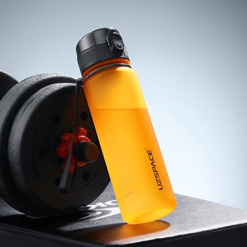 Shopi Vella colorful sports water bottle in orange with black cap next to dumbbell on workout bench