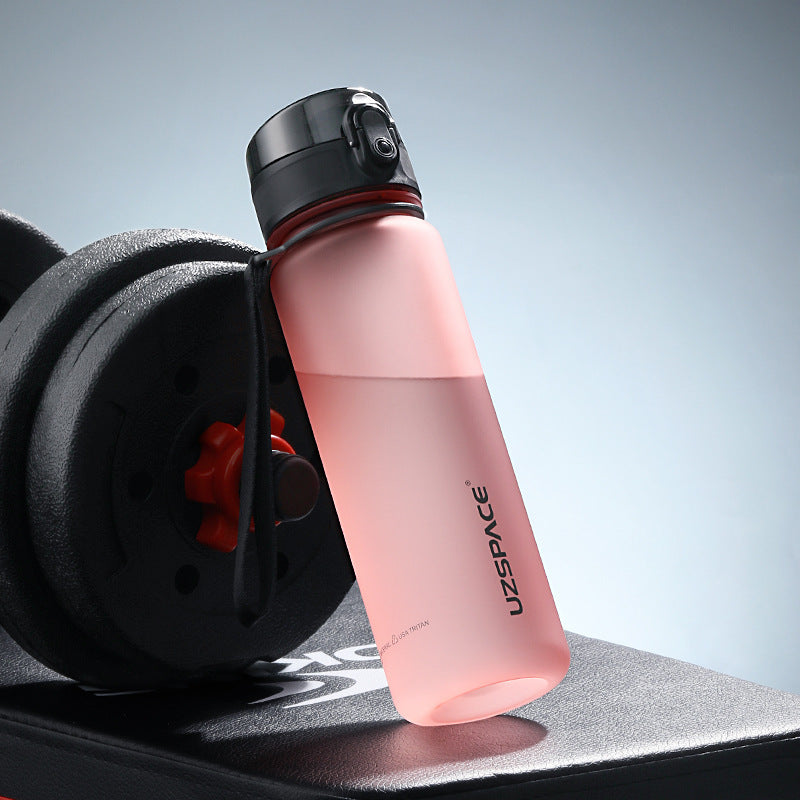 Shopi Vella colorful sports water bottle in pink with black cap next to gym weights