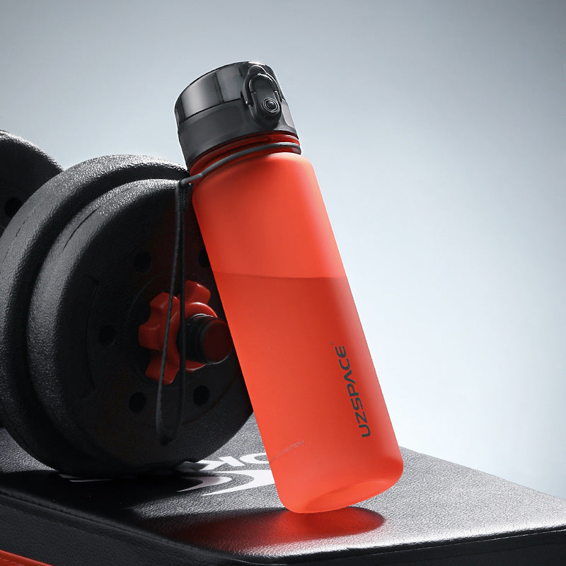Shopi Vella colorful sports water bottle in red next to gym weights on workout bench