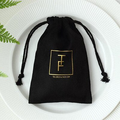 Black velvet jewelry gift bag with gold logo and drawstring closure on white plate