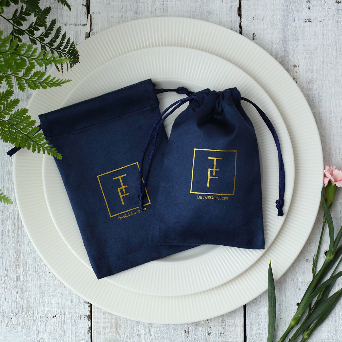 Shopi Vella navy blue velvet jewelry gift bag with gold logo on white plates for home storage