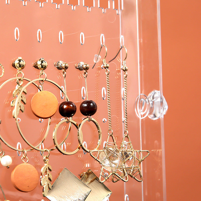 Close-up of clear makeup storage box with drawers holding various gold and wooden earrings