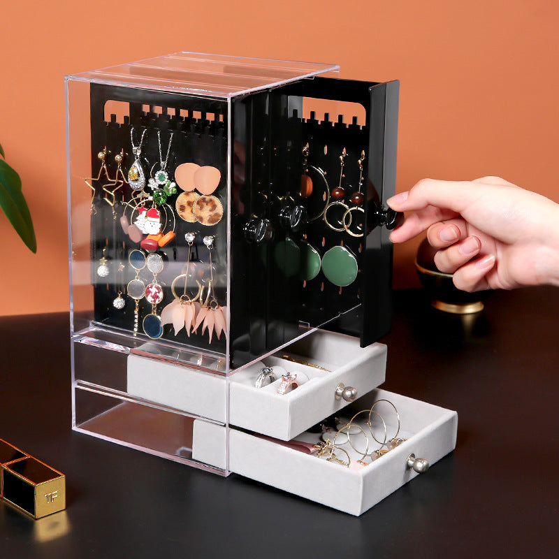 Shopi Vella clear makeup storage box with drawers holding various earrings and jewelry on a black surface