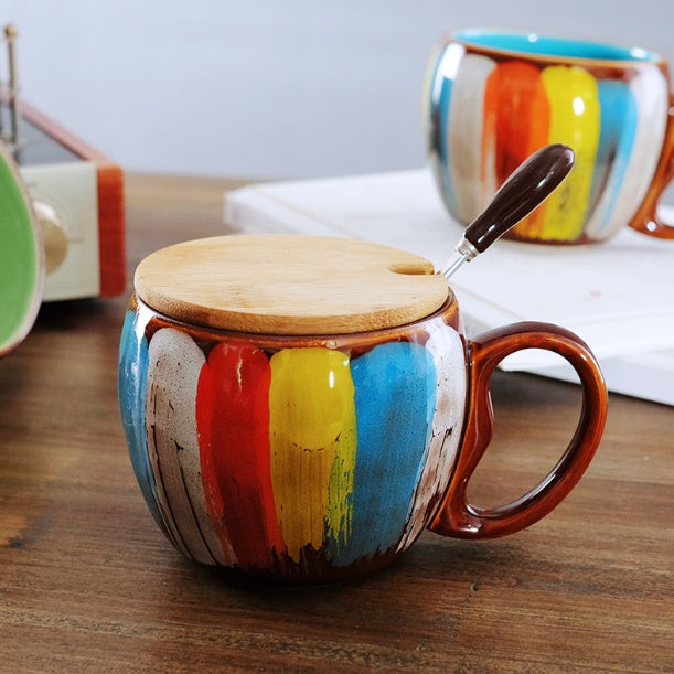 Creative ceramic coffee mug with colorful brushstroke design, wooden lid, and spoon on wooden table