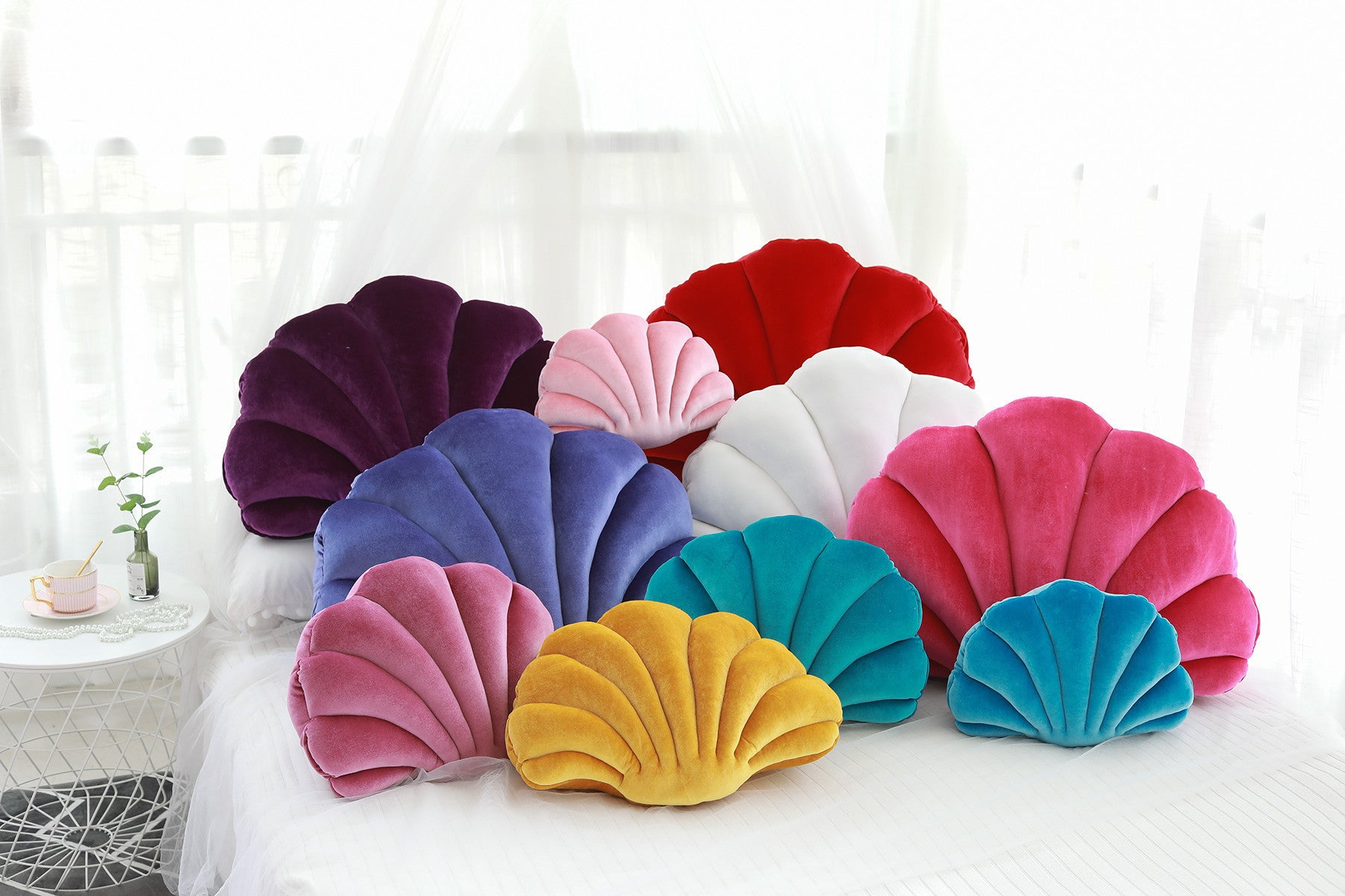 Colorful cute shell nap pillow for kids in various sizes arranged on a white bed by Shopi Vella