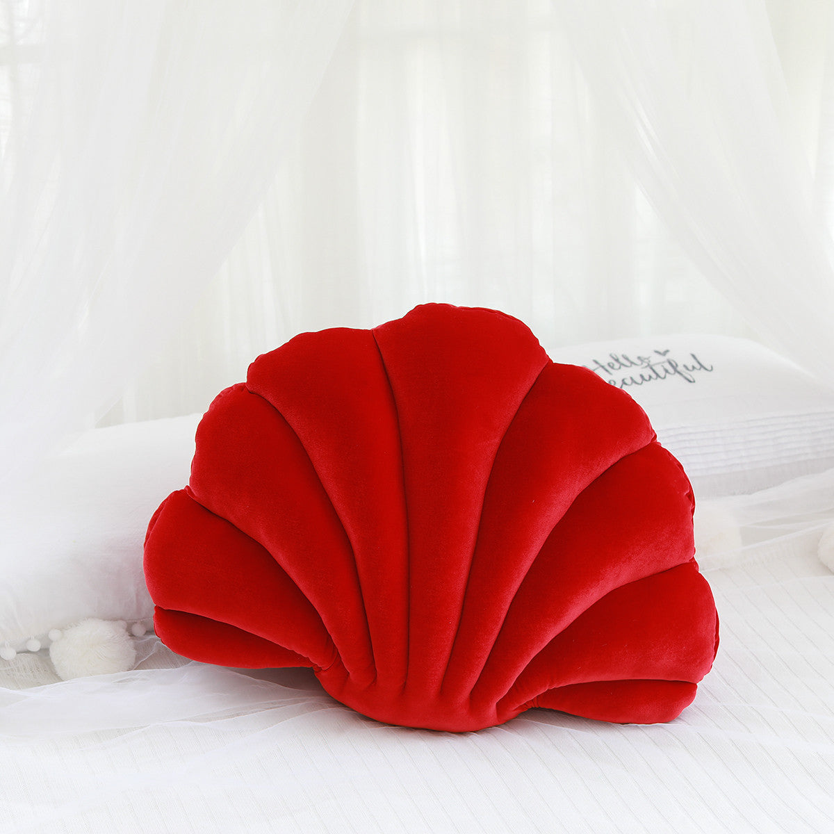 Shopi Vella cute shell nap pillow for kids in vibrant red on a white bed with sheer curtains