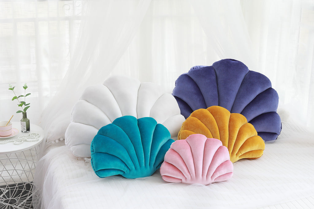 Shopi Vella cute shell nap pillow for kids in various colors displayed on a bed with white bedding