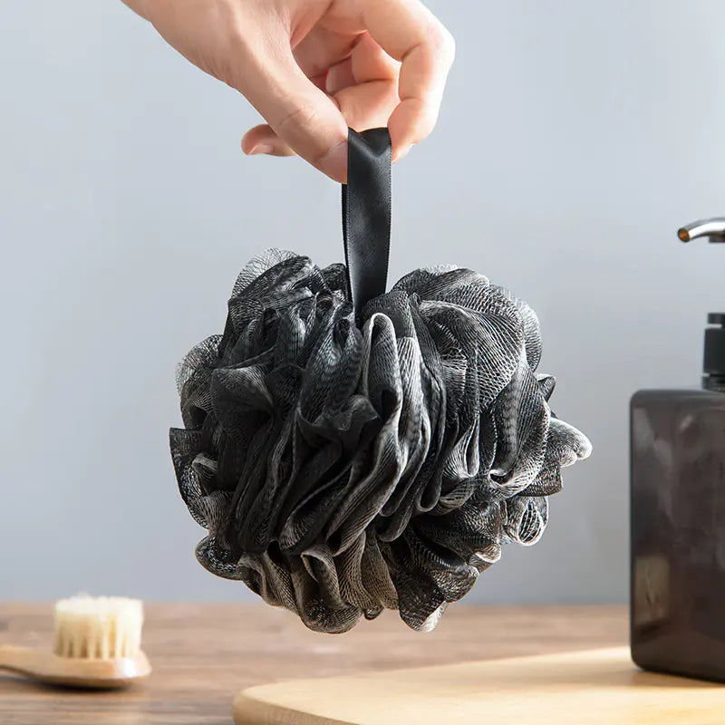 Hand holding black extra large bath sponge for men with hanging loop in bathroom setting