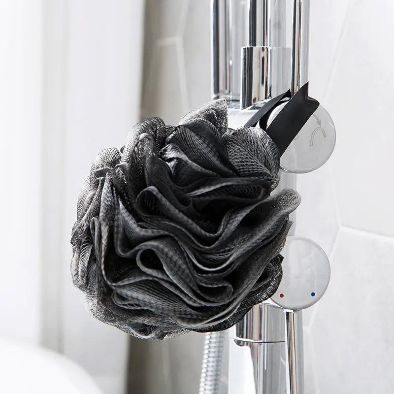 Extra large bath sponge for men in black hanging on a chrome shower fixture in a bathroom