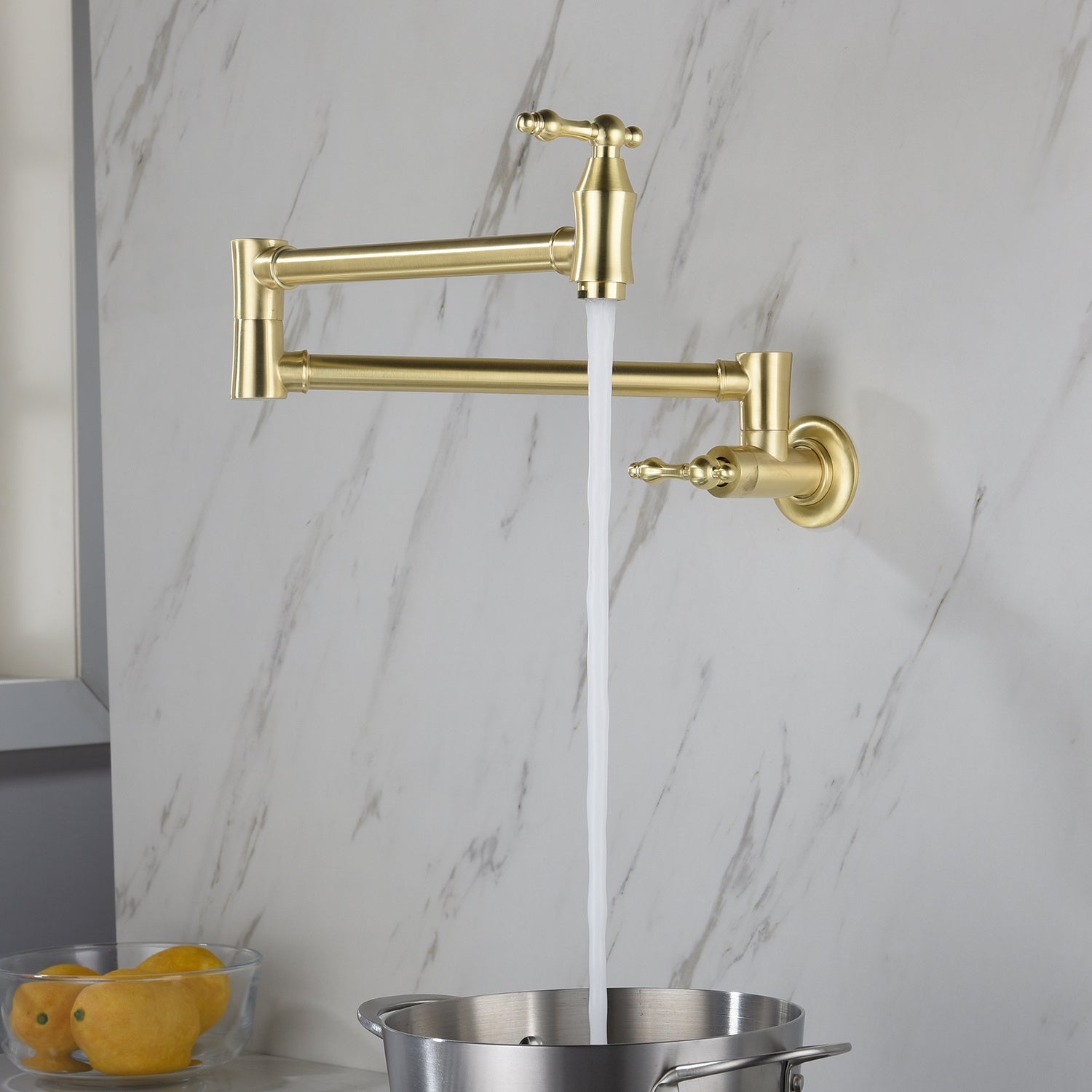 Shopi Vella folding kitchen faucet in gold finish mounted on marble wall with water flowing into pot