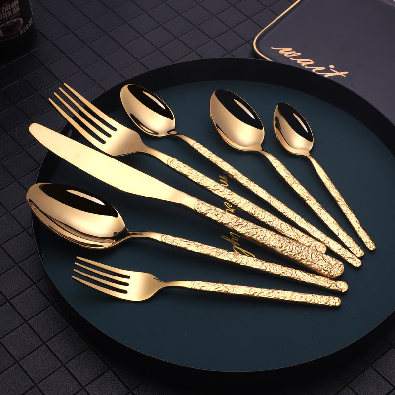 Shopi Vella gold cutlery set for dinner parties with textured handles including knives forks and spoons on black plate