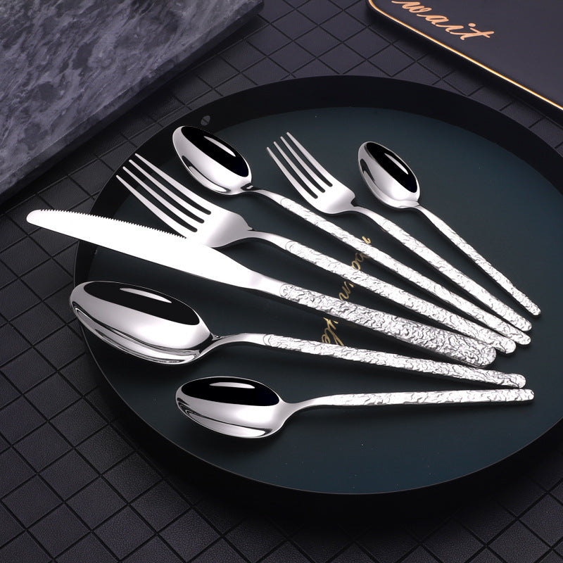 Silver cutlery set with intricate textured handles displayed on a black plate gold cutlery set for dinner parties