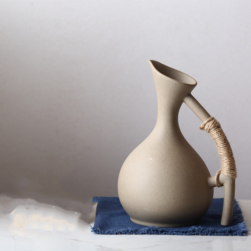 Handcrafted pottery pitcher set with a curved spout and wrapped handle on blue cloth