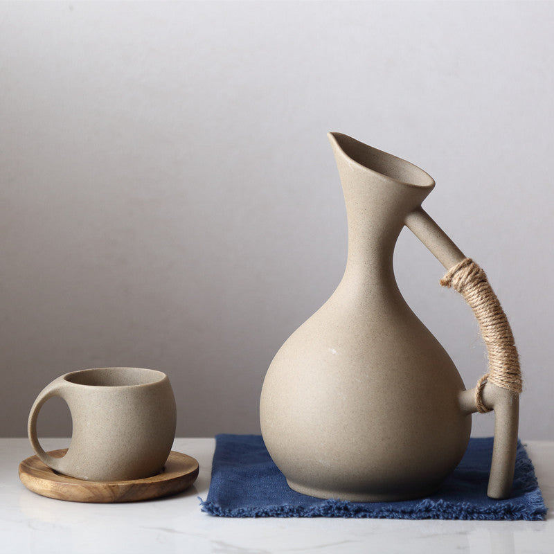 Handcrafted pottery pitcher set with a uniquely shaped pitcher wrapped handle and matching cup on wooden coaster