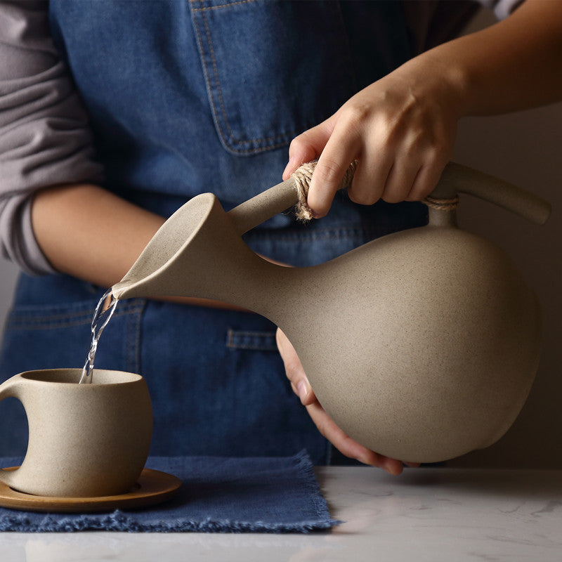 Hand pouring liquid from handcrafted pottery pitcher set into matching mug on blue cloth