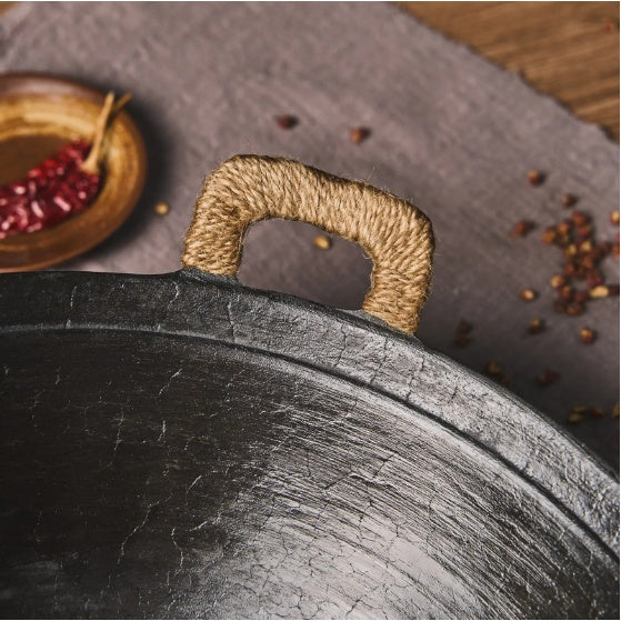 Close-up of Shopi Vella handmade cast iron wok pan with wrapped handle and textured cooking surface