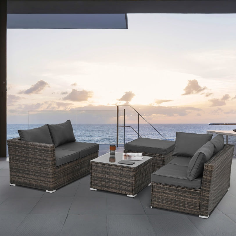 Outdoor wicker patio furniture set with gray cushions on a terrace overlooking the ocean at sunset