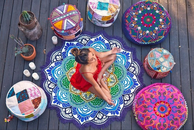 Polygon yoga mat round with colorful mandala design surrounded by decorative round cushions on wooden floor