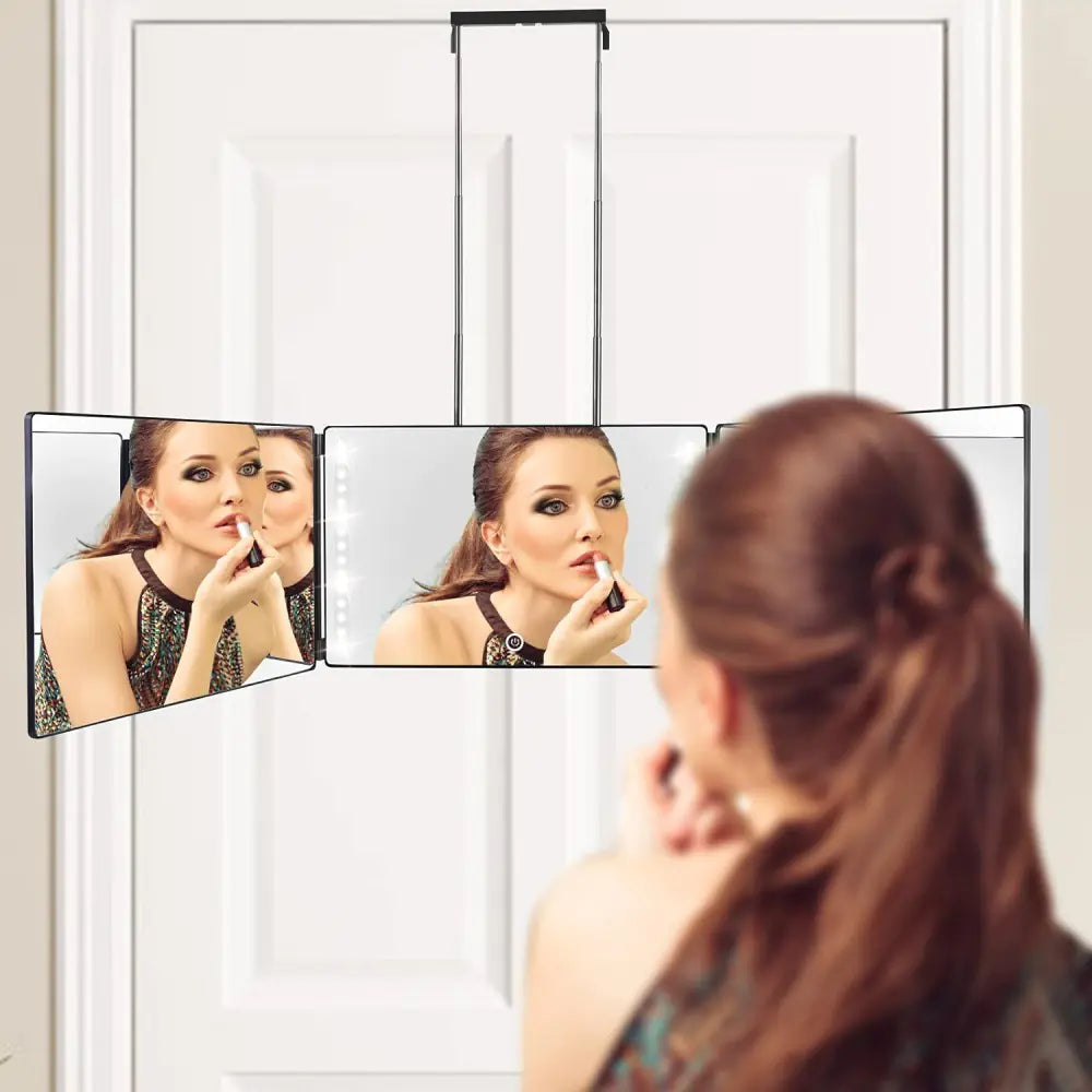Woman applying lipstick using portable LED makeup mirror with three panels hanging on door