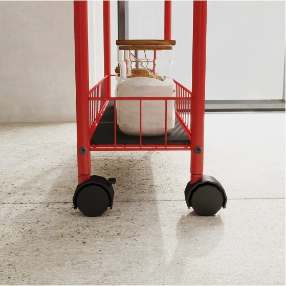 Close-up view of red slim rolling kitchen storage cart with black wheels holding a jar on the bottom shelf