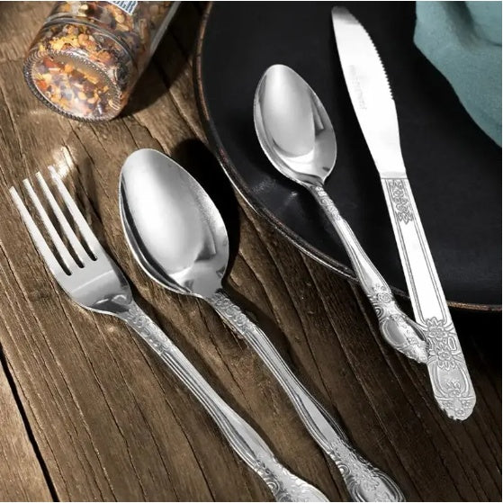 Shopi Vella stainless steel cutlery set with ornate fork, spoons, and knife on wooden table and black plate