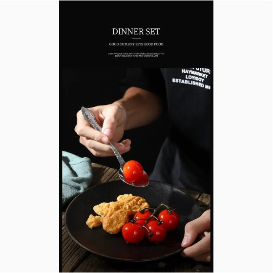 Person using stainless steel cutlery set to place cherry tomatoes on a black plate with chicken