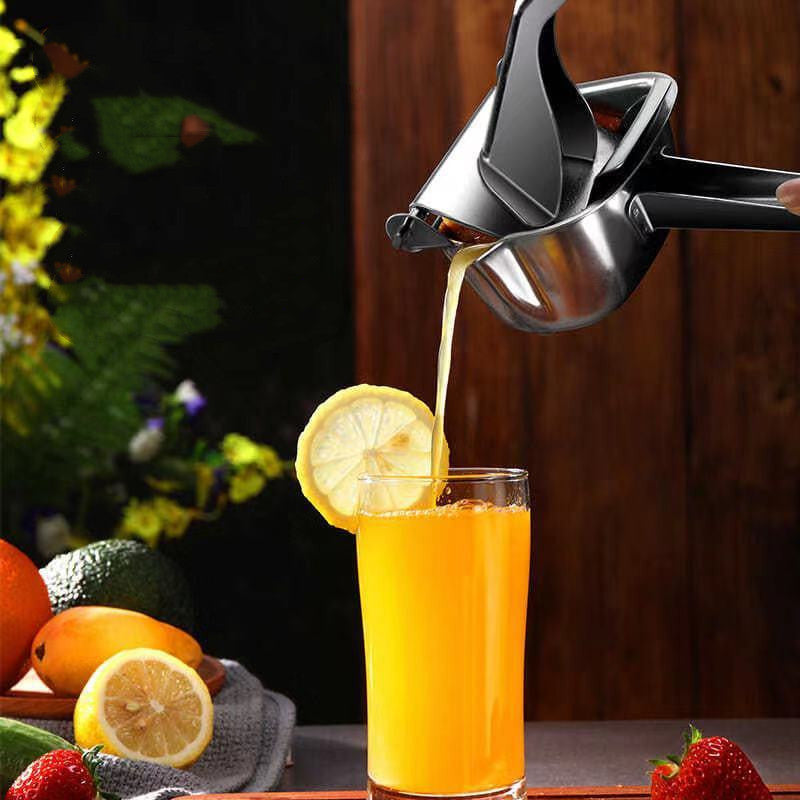 Shopi Vella stainless steel manual juicer pouring fresh orange juice into a glass with lemon slice