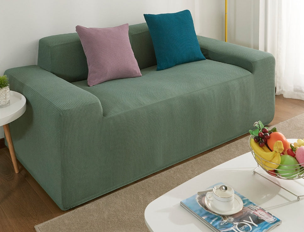 Shopi Vella waterproof sofa slipcover in green protecting a three-seater couch with two decorative pillows