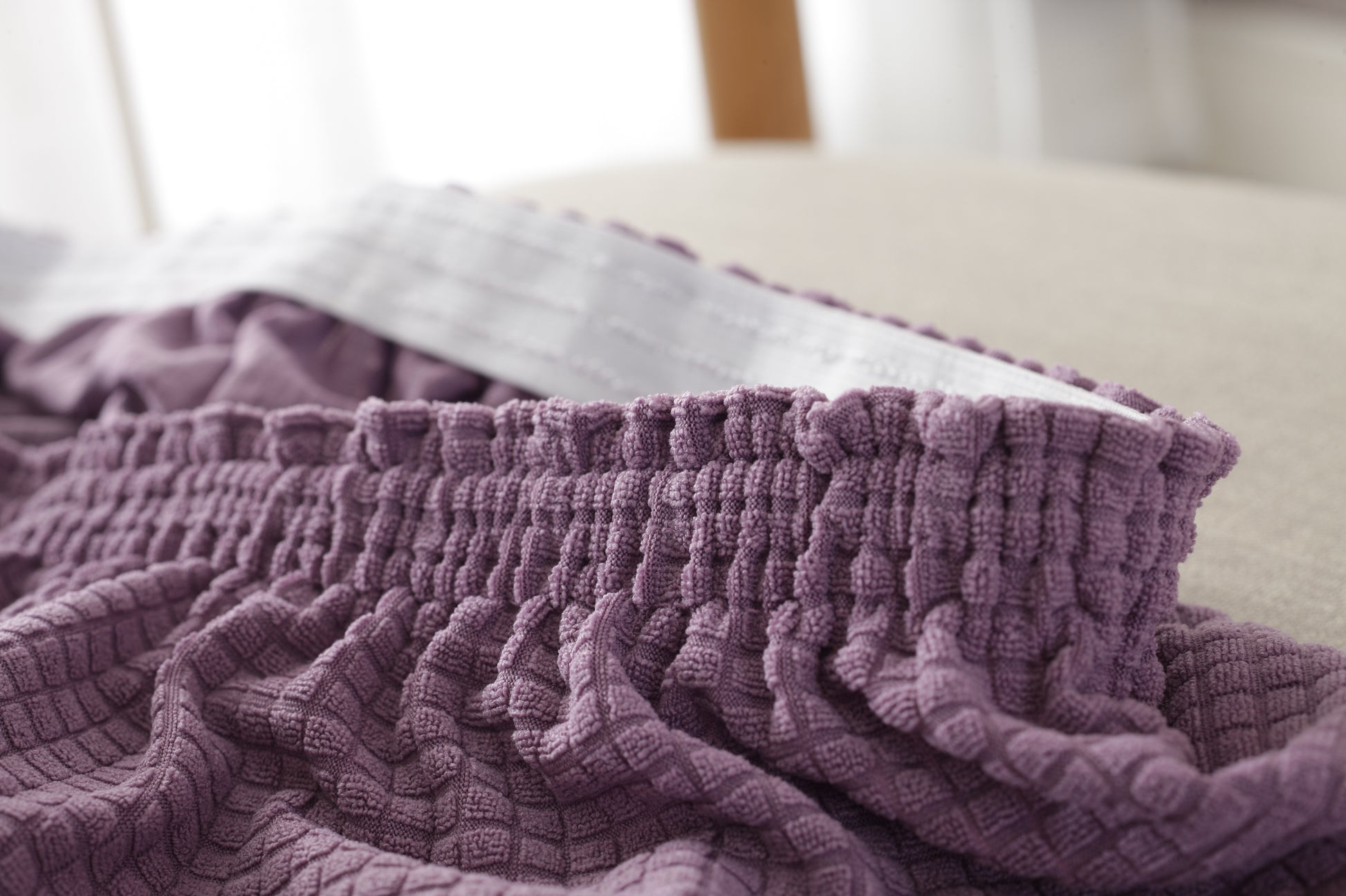 Close-up of purple waterproof sofa slipcover with elastic edge for secure fit on beige sofa