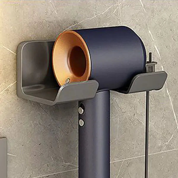 Wall mounted bathroom hair dryer rack in gray holding a black and gold hair dryer on a tiled wall
