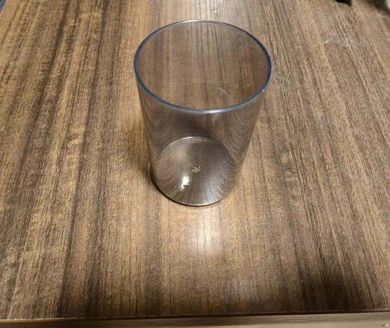Transparent plastic cup for wall-mounted toothbrush holder on wooden surface