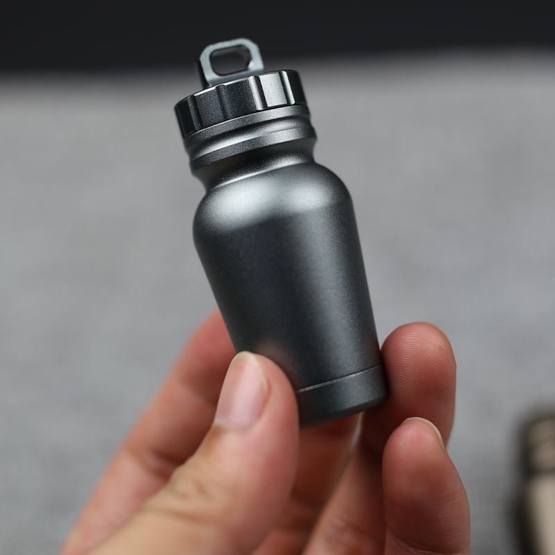 Shopi Vella waterproof medicine bottle for outdoors in compact black design held between fingers