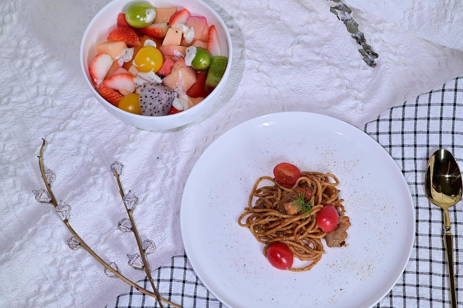White dinnerware set for 4 with bowl of fresh fruit and plate of pasta on textured cloth