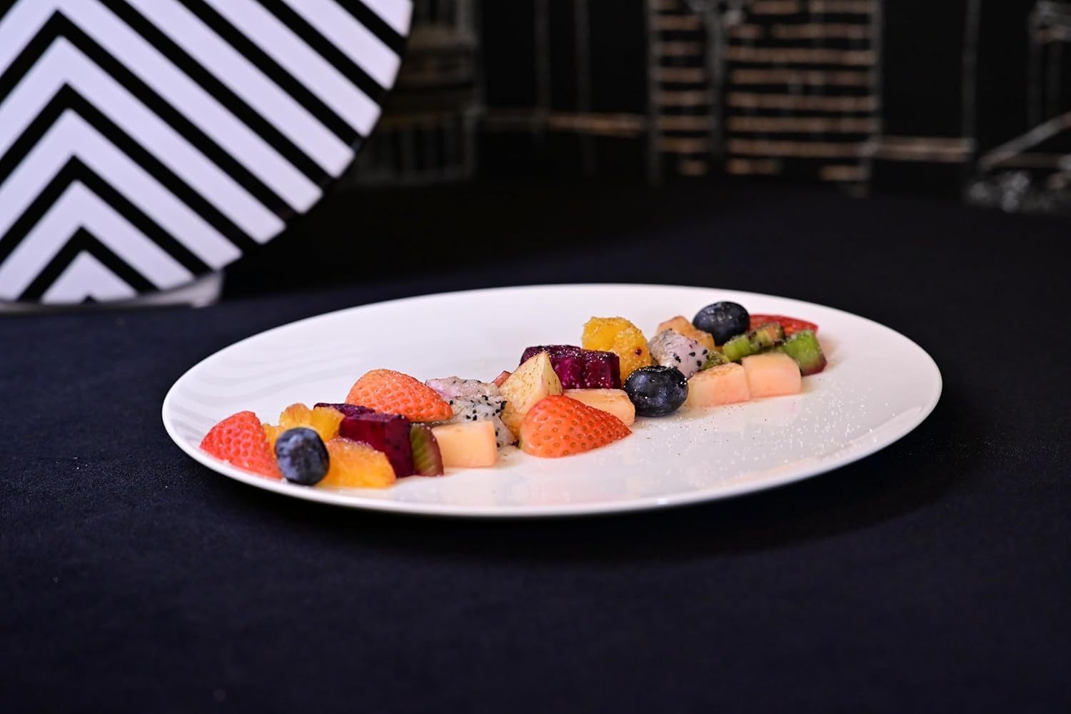 Shopi Vella white dinnerware set for 4 with a white plate holding assorted fresh fruit on a black surface