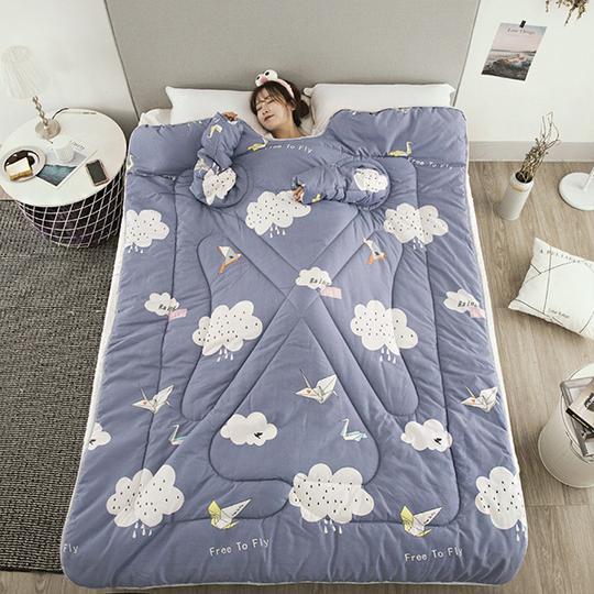 Woman lying on a blue winter quilt with sleeves featuring cloud and bird patterns from Shopi Vella
