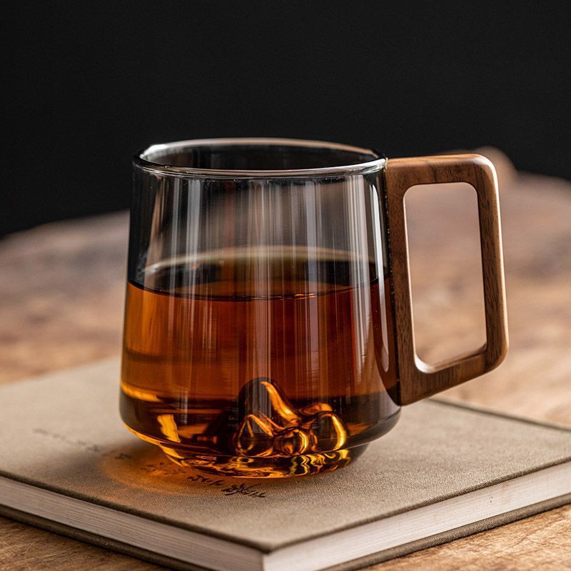 Shopi Vella wooden handle glass cup filled with tea on a closed book in a cozy setting