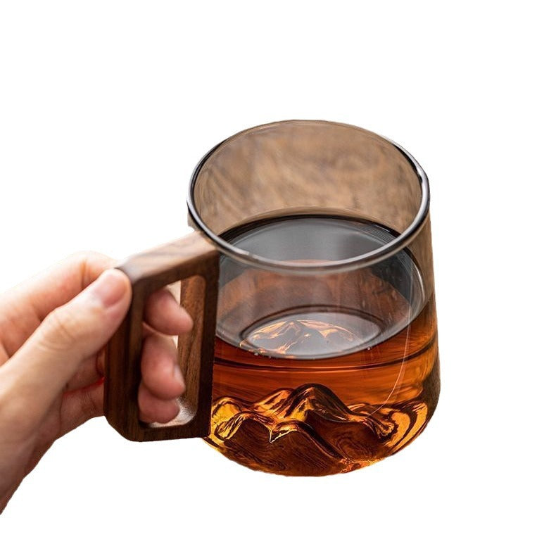 Hand holding a wooden handle glass cup filled with amber liquid for stylish kitchen storage