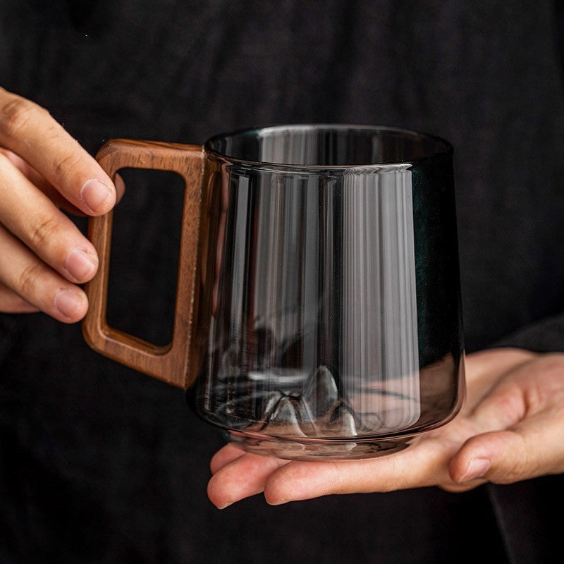 Hand holding Shopi Vella wooden handle glass cup with a transparent dark tinted body for kitchen storage